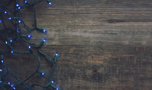 String Of Blue Christmas Lights Over Dark Wood Background, Copy Space