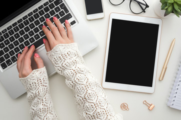 Wall Mural - Top view of woman's hands typing on laptop keypad placed on white office desktop with blank smartphone, decorative plant and supplies. Mock up. Technology devices view from above. Office equipment.