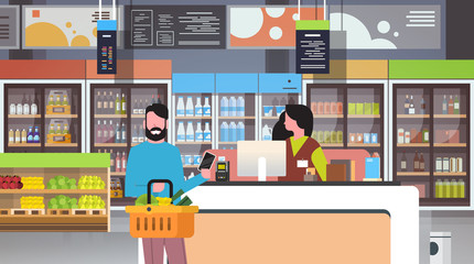 retail woman cashier at checkout supermarket man customer holding basket food paying smartphone shopping concept grocery market interior flat horizontal