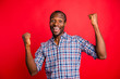 © deagreez - Portrait of nice handsome cheerful cheery glad optimistic guy wearing checked shirt showing winning gesture holding fists isolated over bright vivid shine red background