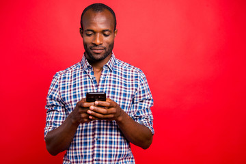 Portrait of he nice handsome attractive cheerful guy wearing checkered shirt holding in hands cell playing game isolated over bright vivid shine red background