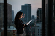 © ReeldealHD images - Businesswoman working late using digital tablet with city skyline in background