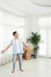 © DragonImages - Cheerful Asian man standing in light spacious room of new real estate holding hands apart excited with space