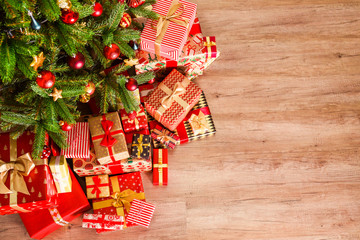 Top view composition of Christmas tree branches with stack of different presents in colorful festive wrapping tied with bow. Pile of gifts under spruce tree on wooden floor. Background, copy space.