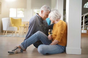 Relaxed senior couple sitting on floor in modern home with glass of wine