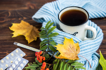 Wall Mural - Tea cup with thermometer, blue scarf and autumn leaves on wooden background. Flu season in autumn, disease.