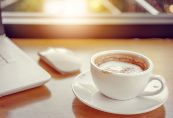 Selective focus, Cup of coffee latte art in coffee shop with blurred laptop background.