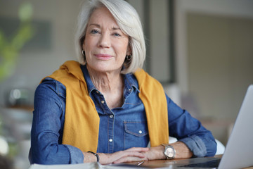  Beautiful senior woman looking pensive at home with laptop