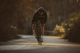 Fototapeta Miasta - Professional road bicycle racer in action. Men cycling mountain road bike at sunset.