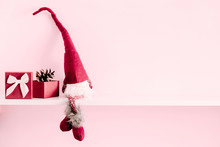 Red Sitting Christmas Elf With Pointed Cap On White Shelf And Pink Wall 