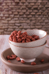 Two ceramic bowls full of peanuts coated by sweet red dough