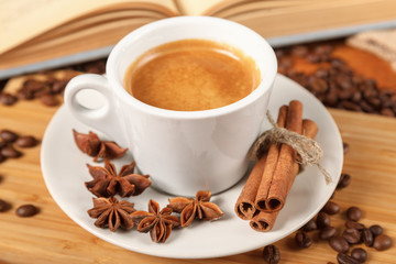 Wall Mural - Coffee break a Cup of hot coffee and a book on a wooden table. A white Cup of black coffee surrounded by a small amount of roasted coffee beans, cinnamon, anise and an open book