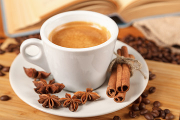 Wall Mural - Coffee break a Cup of hot coffee and a book on a wooden table. A white Cup of black coffee surrounded by a small amount of roasted coffee beans, cinnamon, anise and an open book