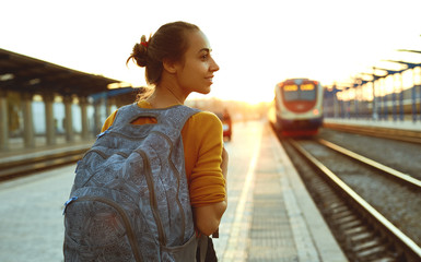 portrait of a young woman traveler with small backpack on the railway stantion