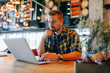 © Dusan Petkovic - Young Caucasian bearded freelancer using laptop and sitting in cafe. One hand on keyboard and other on the chin. In ears earphones. Self employing concept.