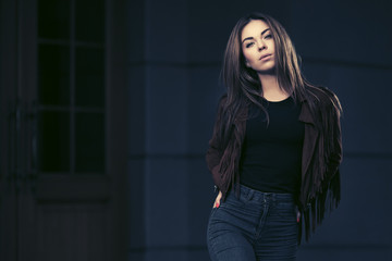 Happy young fashion woman in leather jacket walking on city street