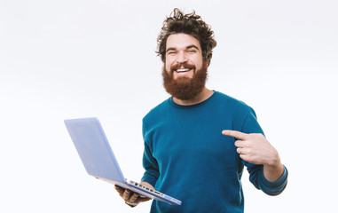 Portrait of cheerful bearded man pointing at laptop over white background, studio shot
