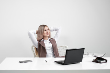 Caucasian girl sitting at the table at the computer in the office. Rejoices and smiles.