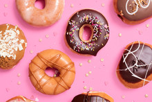Overhead View Of Various Donuts With Confetti Arranged On Pink Background