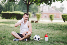 Smiling Young Man Wiping Neck While Sitting On Soccer Field At Park
