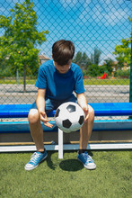 Boy Holding Soccer Ball While Sitting On Bench By Fence At Dugout