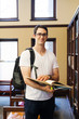 © Cavan Images - Portrait of confident male student with backpack holding book while standing by shelf in library
