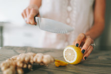 A Woman Cutting Lemon And Ginger On A Cutting Board.