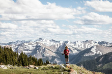 Male Hiker With Dog Standing On Mountain Against Cloudy Sky During Sunny Day