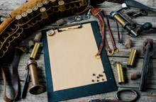 Clipboard With Paper On Old Wooden Background. Hunting Equipment On Vintage Desk. Hunting Belt With Cartridges, Top View