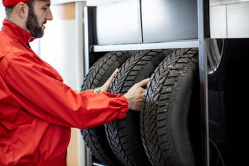 Wall Mural - Car service worker in red uniform taking new wheel from the shelves of the wheel store