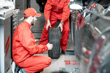 Wall Mural - Two car service workers in red uniform changing wheel of a sport car at the tire mounting service