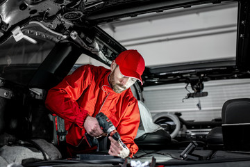 Wall Mural - Handsome auto service worker in red uniform disassembling new car interior making some improvements