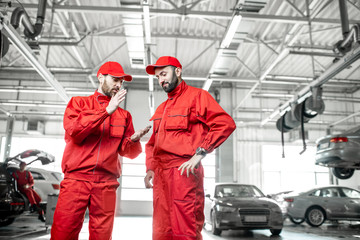 Wall Mural - Two auto mechanics in red uniform talking together during the break at the car service