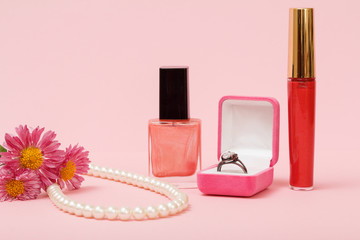 Box with ring, nail polish, lipstick and flowers on a pink backg