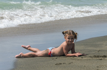 Adorable baby girl playing at the sea while relaxing on a bright sunny day on a sandy beach