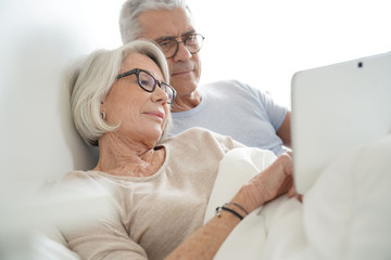 Wall Mural - Senior married couple relaxing in bed looking at tablet