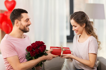 valentines day, couple, relationships and people concept - happy man giving woman flowers and present at home