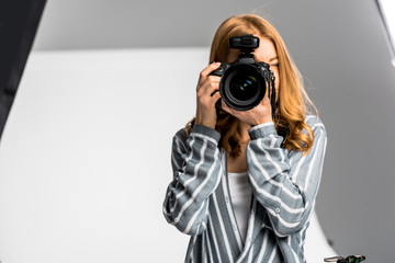 Wall Mural - beautiful young female photographer shooting with professional camera in studio