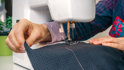 Wall Mural - Closeup of seamstress hands working with clothing item on a sewing machine