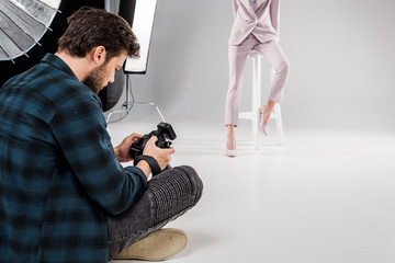 Wall Mural - photographer sitting with camera and young model posing in photo studio