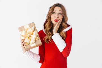 Wall Mural - Portrait of optimistic woman 20s wearing Santa Claus red costume smiling and holding present box, isolated over white background