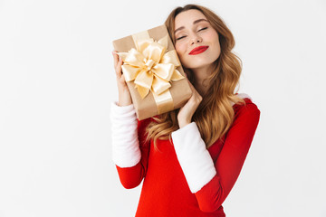 Wall Mural - Portrait of cute woman 20s wearing Santa Claus red costume smiling and holding gift box, isolated over white background