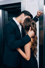 man in suit passionately kissing and embracing woman near elevator