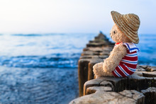 Nostalgic Holidays At The Sea / Teddy Bear At Summer Vacation Sit On Row Of Wooden Groynes, Wear Straw Hat And Striped Sailor Suit, Take A Look Toward Blue Water Horizon (copy Space)
