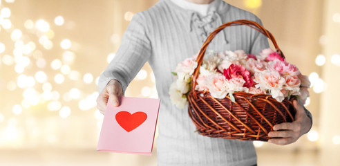 valentines day, delivery and people concept - close up of man holding basket of flowers with greeting card over festive lights