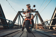 Close-up Young Woman Sitting On The Motorbike. Stop Over On The New Repaired Vintage Wooden Bridge. Biker Background. Outdoor Extreme Activity. Wild Road Adventure.