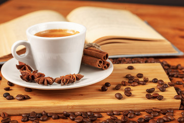 Wall Mural - Coffee break with a Cup of hot strong coffee on a wooden table with an open old book covered with cloth. A white Cup of black coffee surrounded by a small amount of roasted coffee beans