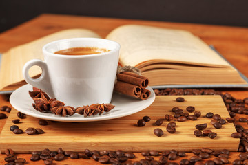 Wall Mural - Coffee break with a Cup of hot strong coffee on a wooden table with an open old book covered with cloth. A white Cup of black coffee surrounded by a small amount of roasted coffee beans