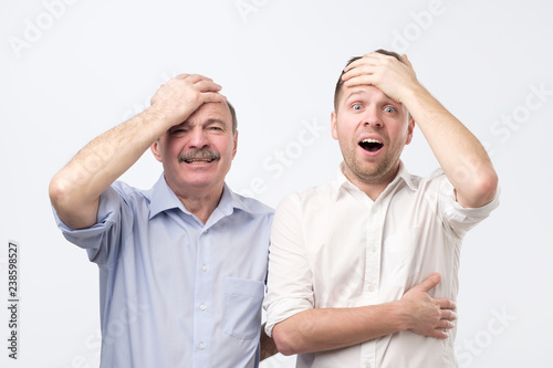 Fotografie, Obraz Stunned emotive two men keep jaw dropped, holding hand on head, wonder seasonal