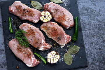 Raw pork steaks with spices on a stone board for a presentation. Pork steaks are marinated in spices on the board.